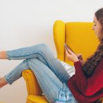 Ecommerce - woman in red sweater and blue denim jeans sitting on yellow couch