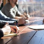 Business Consulting - people sitting on chair in front of table while holding pens during daytime